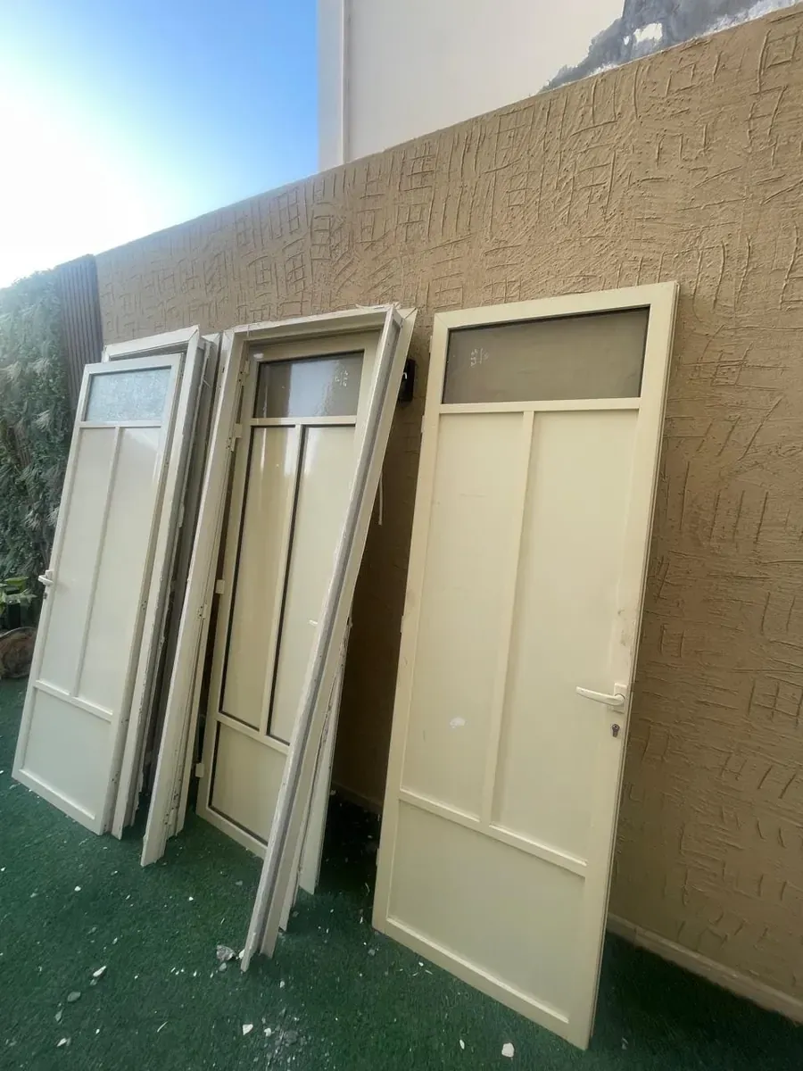 ثلاثة أبواب ألمنيوم مسندة إلى جدار مطلي